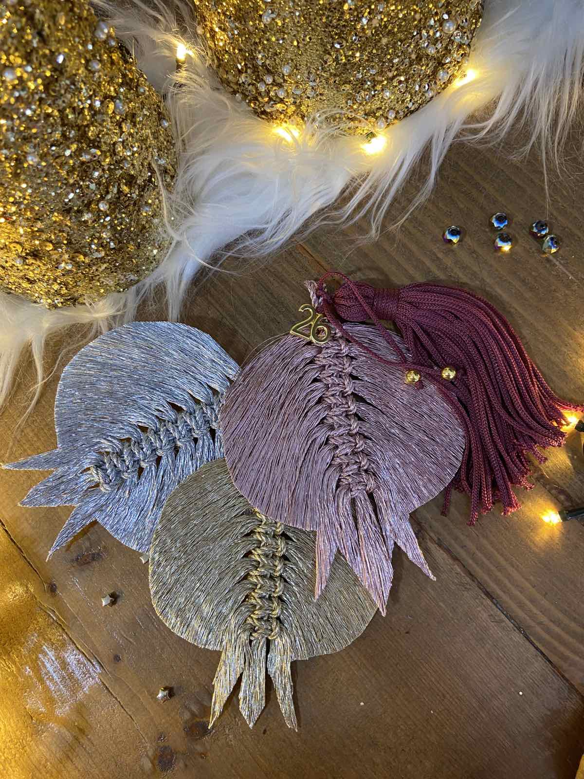 Χειροποίητο μακραμέ γούρι 2026 σε ροζ μεταλλιζέ με βουργουνδί φούντα και χρυσό “2026”, από το Capricorn Creations.