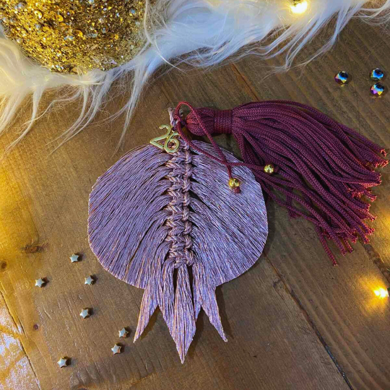 Χειροποίητο μακραμέ γούρι 2026 σε ροζ μεταλλιζέ με βουργουνδί φούντα και χρυσό “2026”, από το Capricorn Creations.